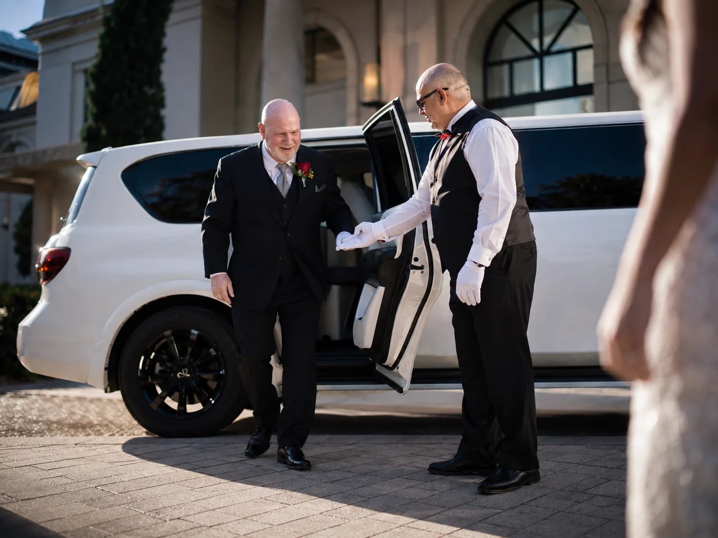 A Danaro chauffeur assisting a wedding guest from a white stretch limousine.