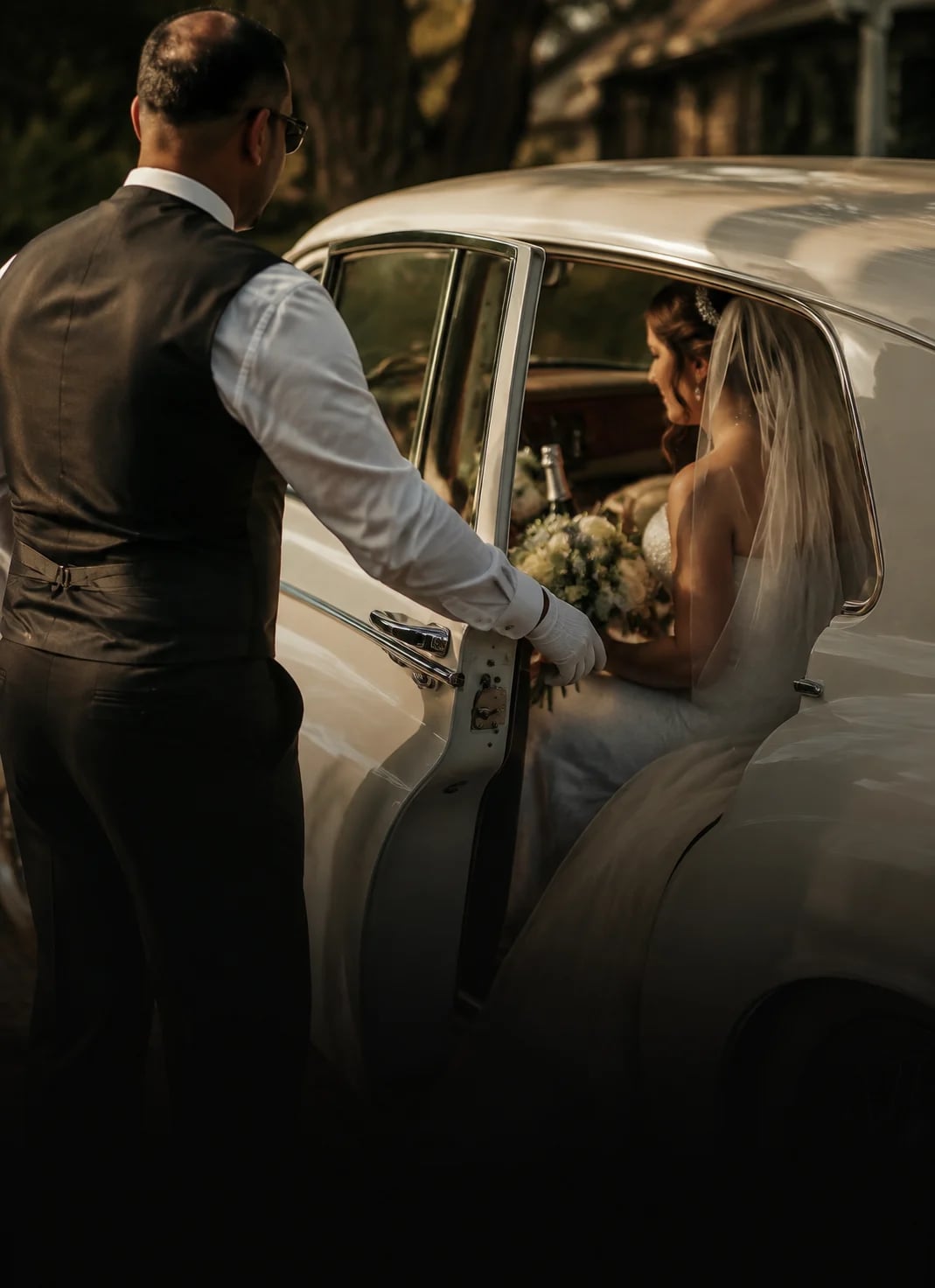 A white-glove Danaro chauffeur opening a classic wedding car door for a bride.